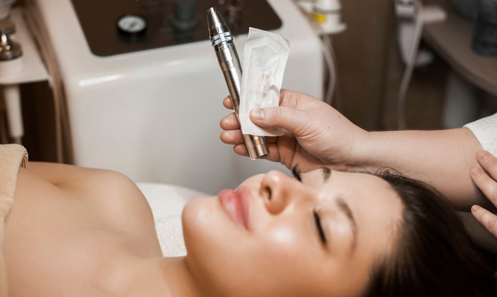 Cosmetologist hands holding a dermapen for future microneedling procedure on womans face to which is leaning bed with closed eyes | The Skin Refinery in Fayetteville, TN